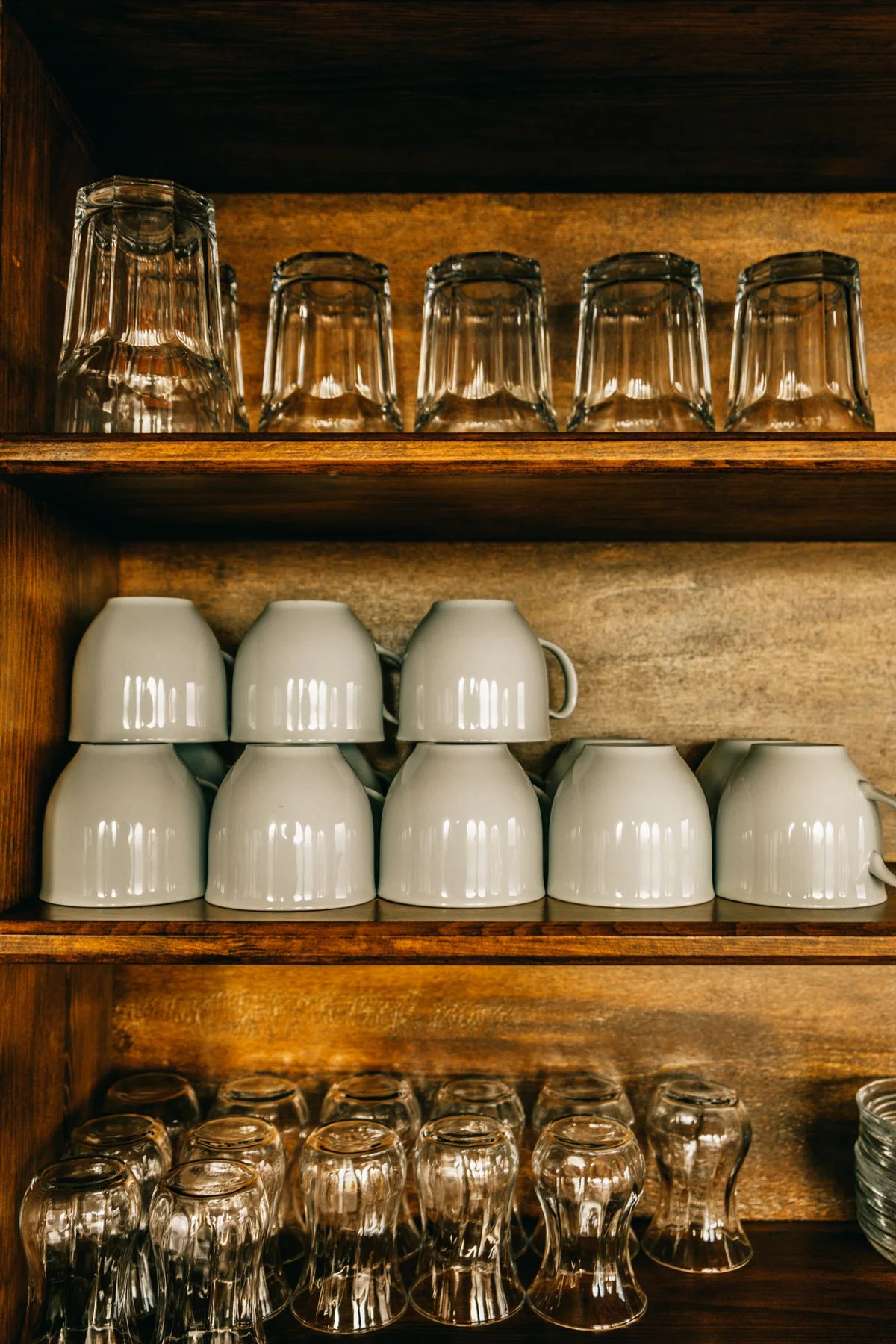 Drinking glasses and cups stored on wooden cupboard shelves.