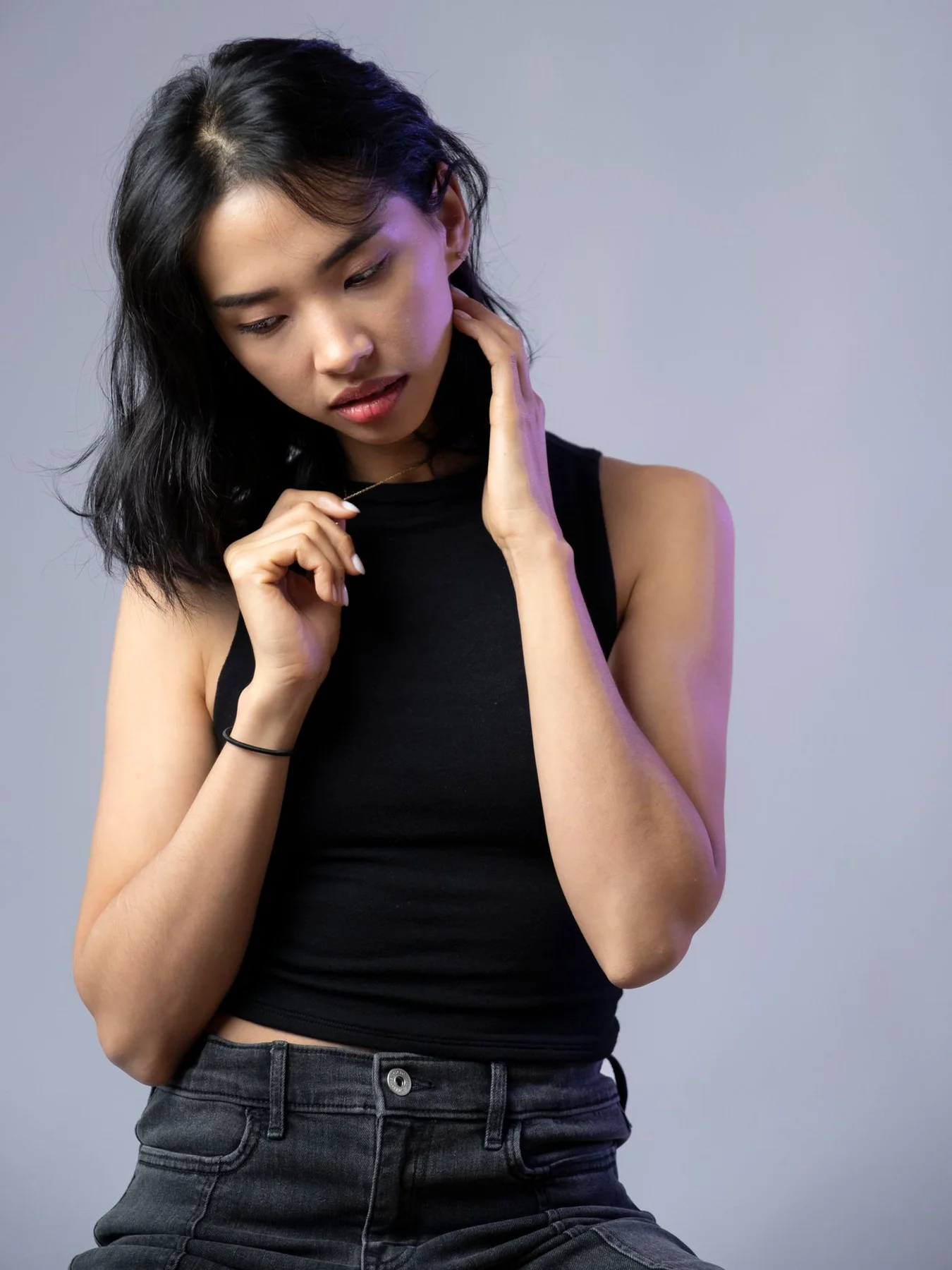 A woman wearing a black tank top against a grey studio background.