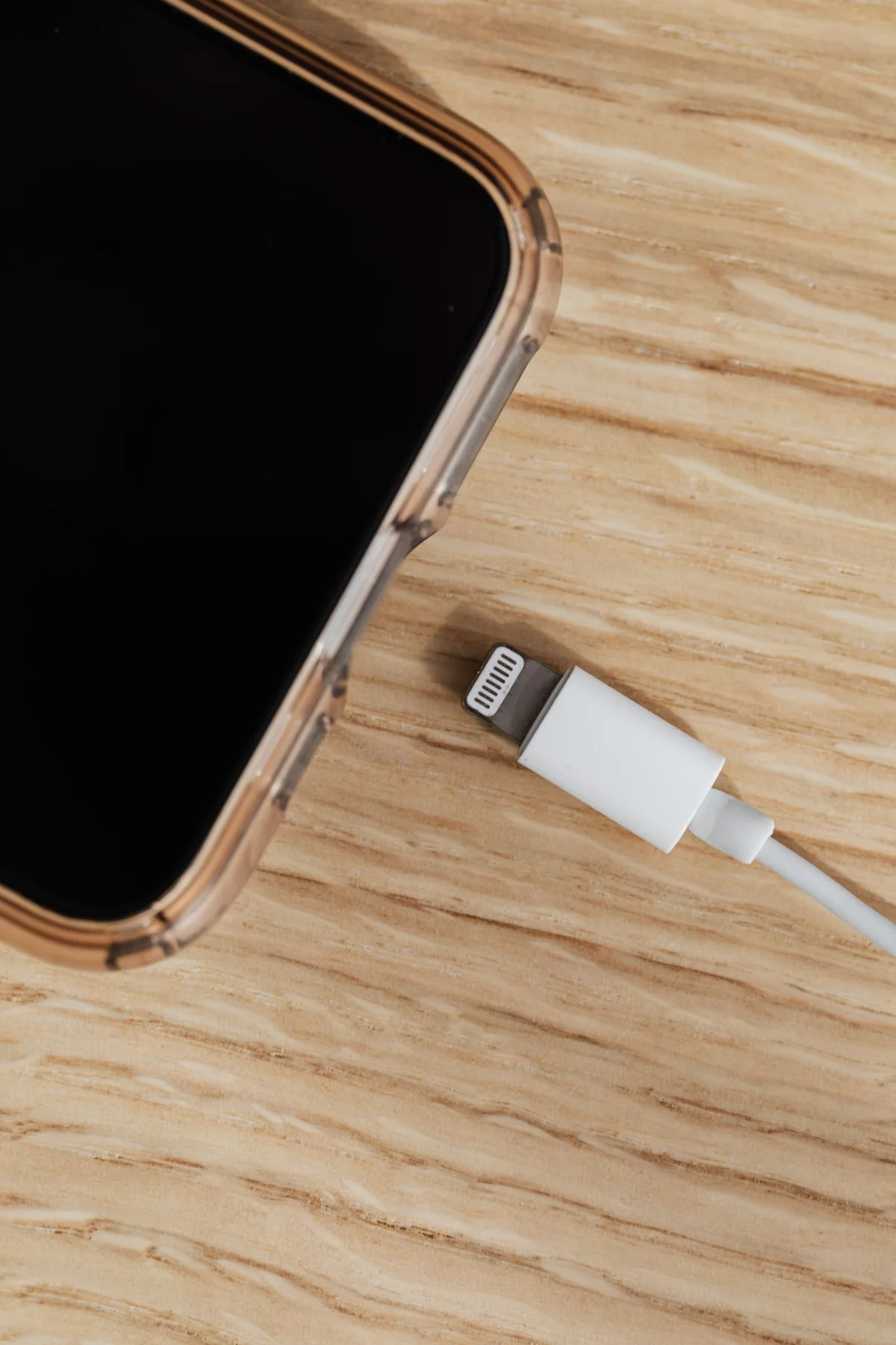 A phone and white charging cable on a wooden table.