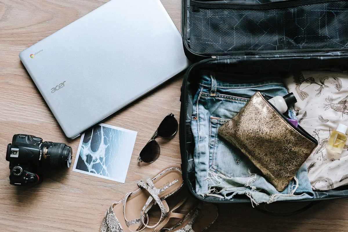 An open suitcase with jeans, sandals, sunglasses and a small pouch