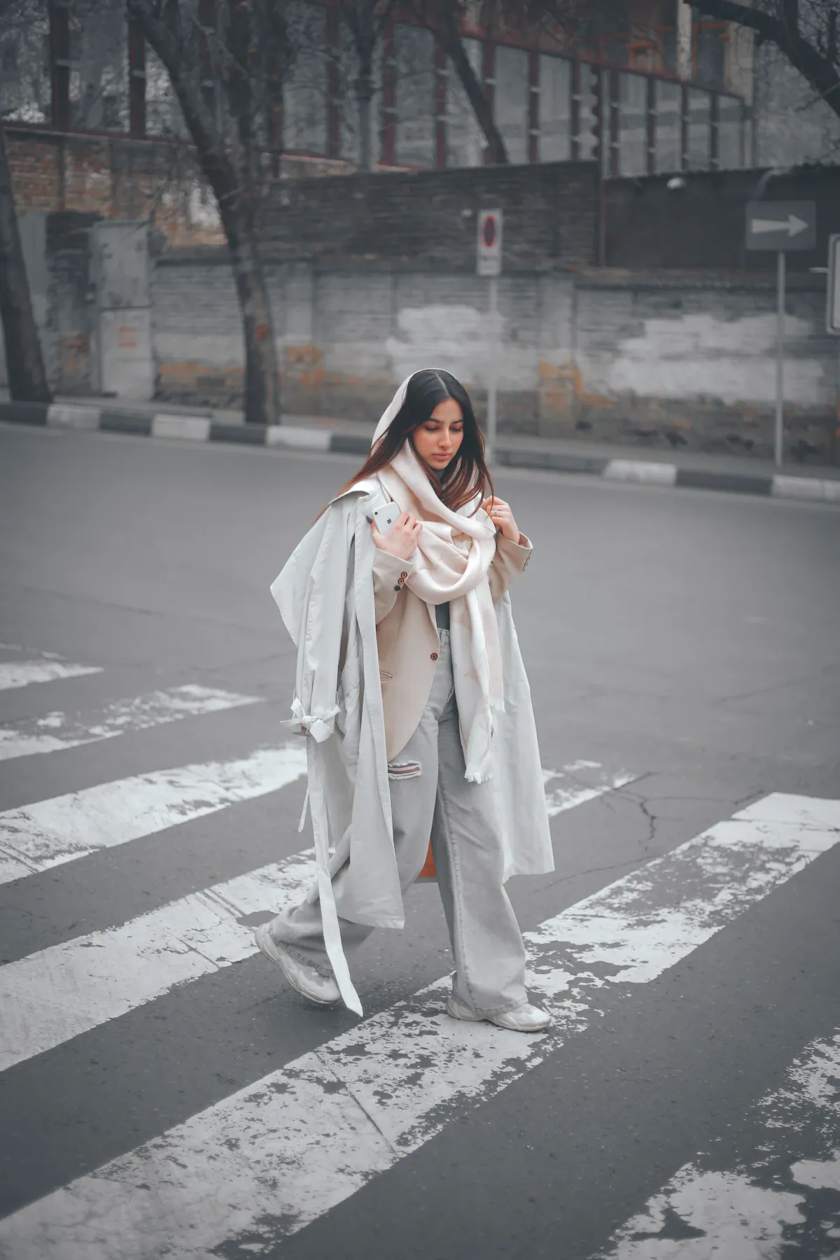 A woman in a light coat and scarf crossing a city street