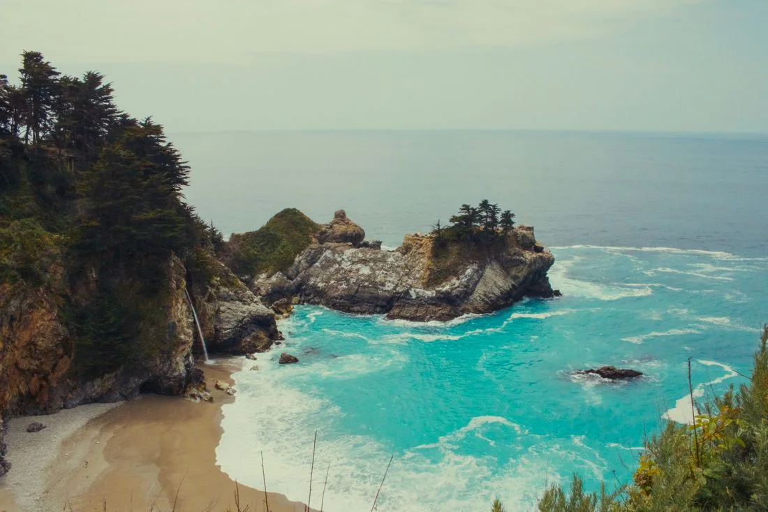 Rocky coastal cliffs around a pale sandy cove and blue-green water.