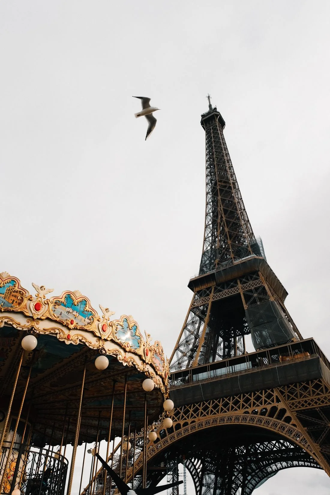 The Eiffel Tower beside a carousel under a pale sky.