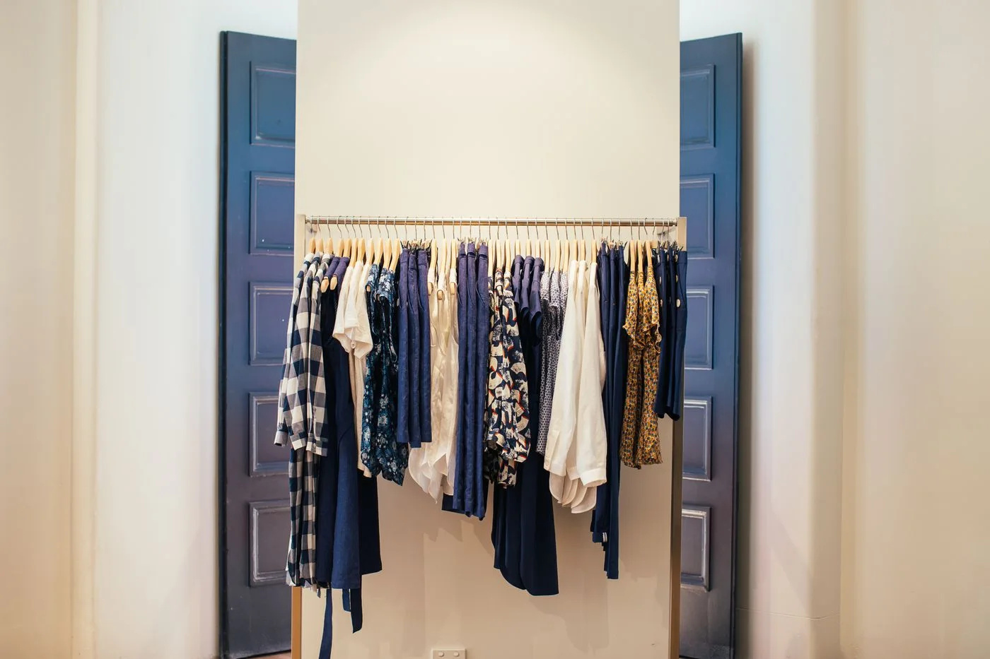 Pale and dark clothes arranged on a rail between tall doors.