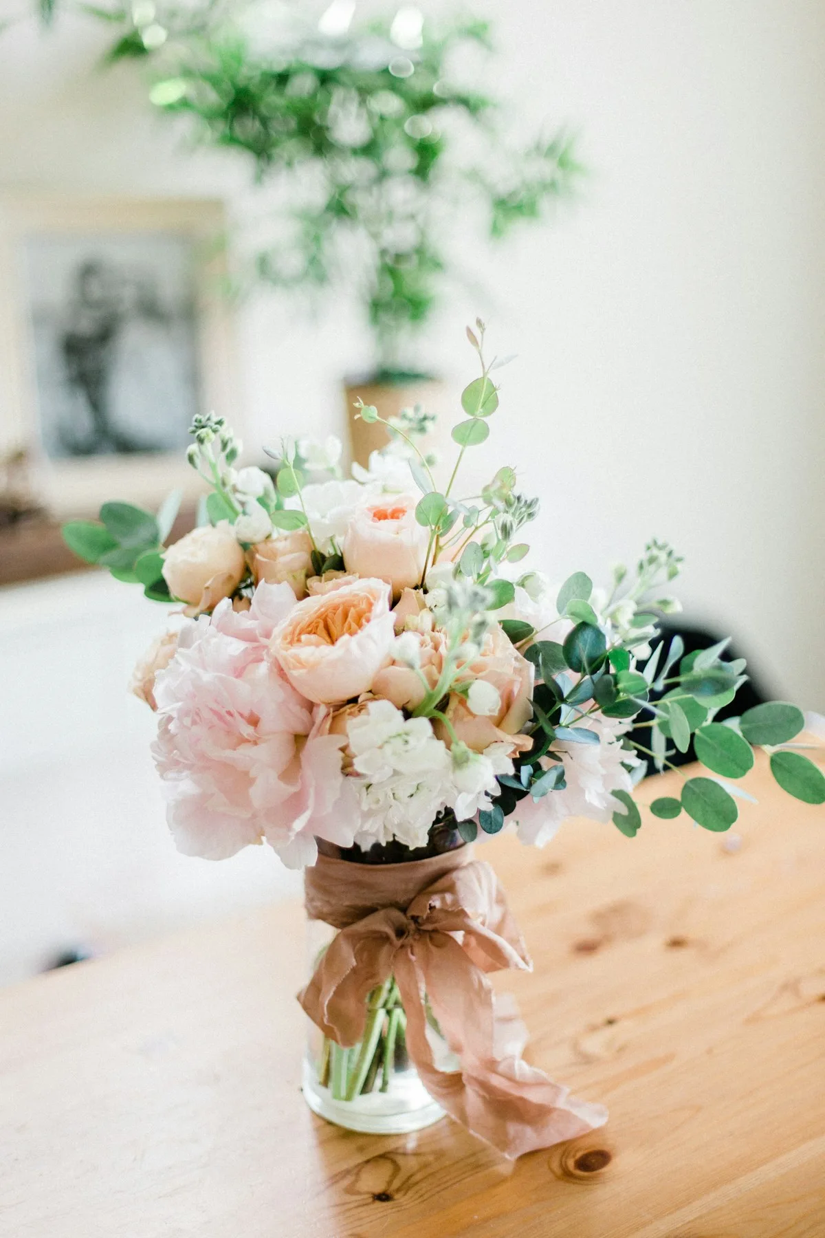 Pale pink and white flowers with green foliage in a clear vase.