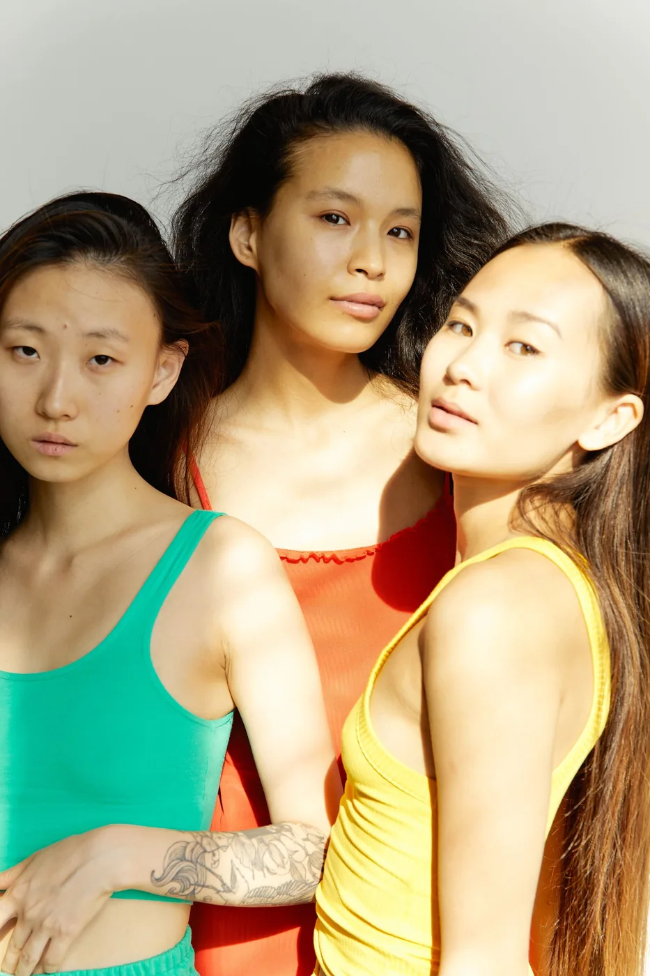Three women wearing green, red and yellow tops together.