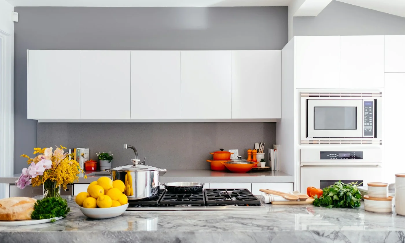 A pale kitchen with food, dishes and cookware on the counter.