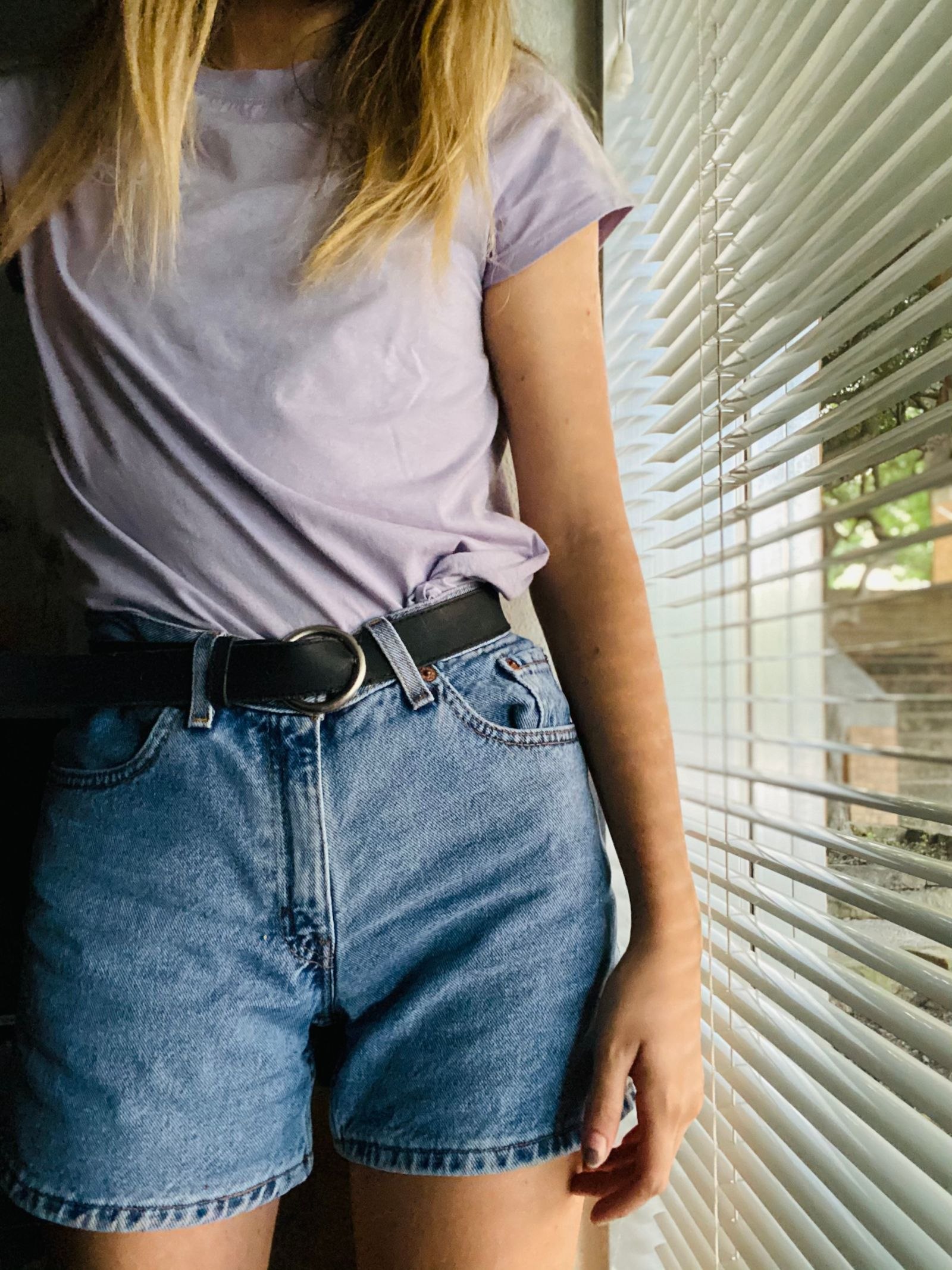 Close-up of a black belt worn with blue denim beside window blinds