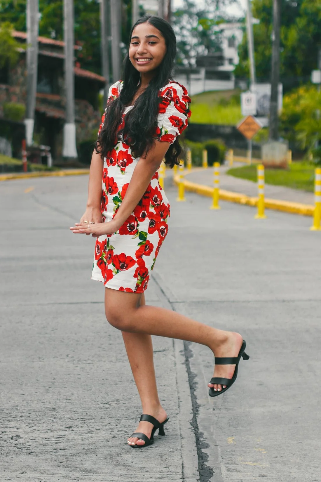A woman wearing a red-and-white floral dress on a paved street.