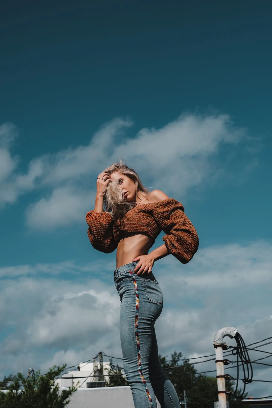 A person wearing a brown top and jeans beneath a blue sky.