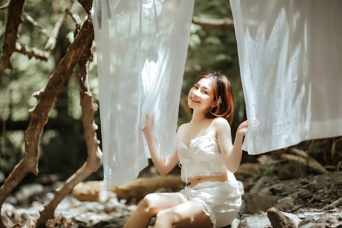 A woman wearing a pale summer dress beside hanging white fabric outdoors.
