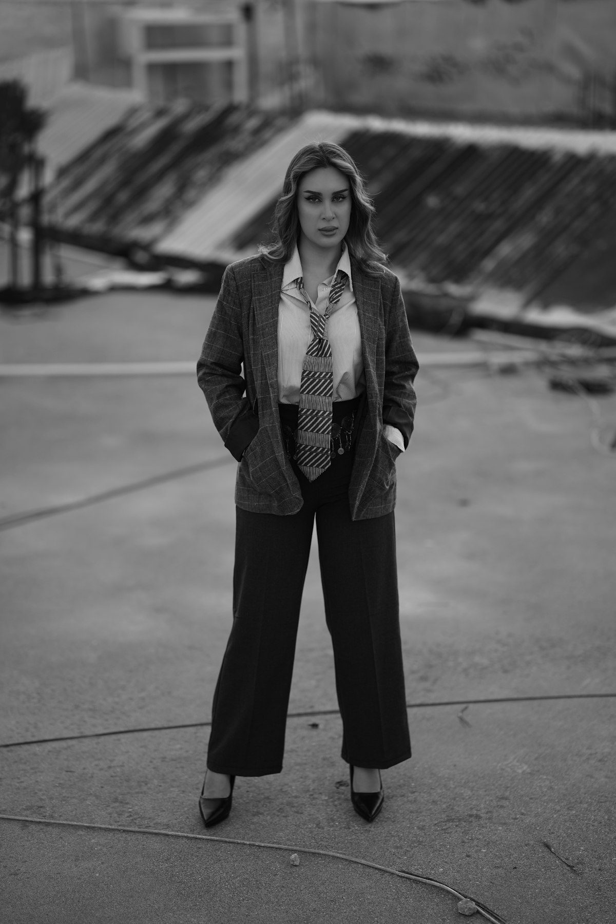 A black-and-white portrait of a person in a blazer and wide trousers.