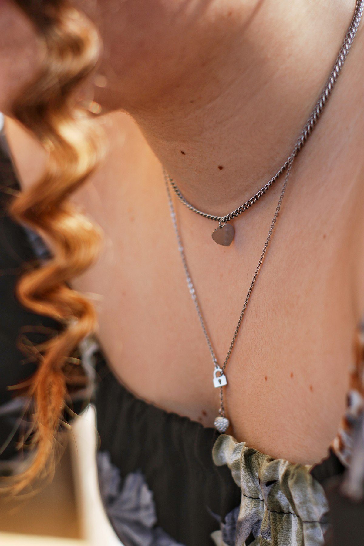 Layered necklaces above a dark lace-edged neckline.