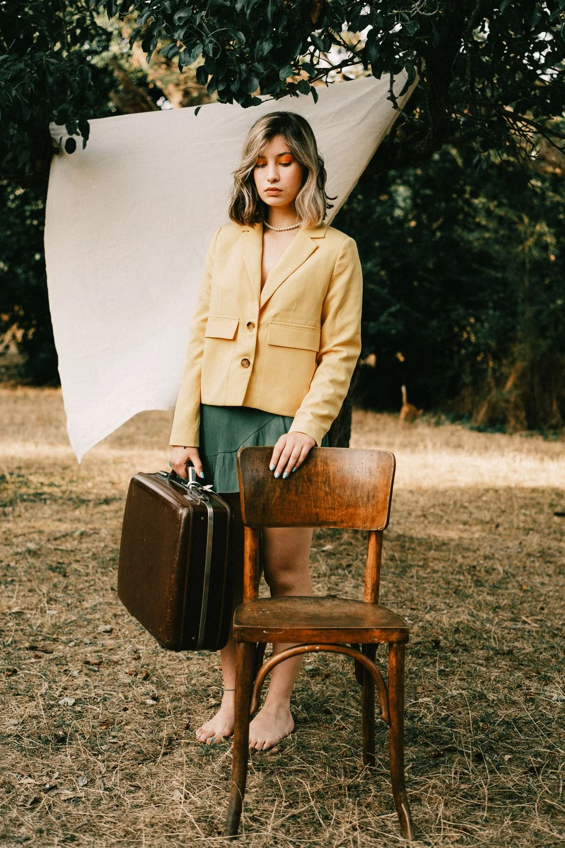 A woman in a pale yellow jacket holding a dark structured case outdoors.