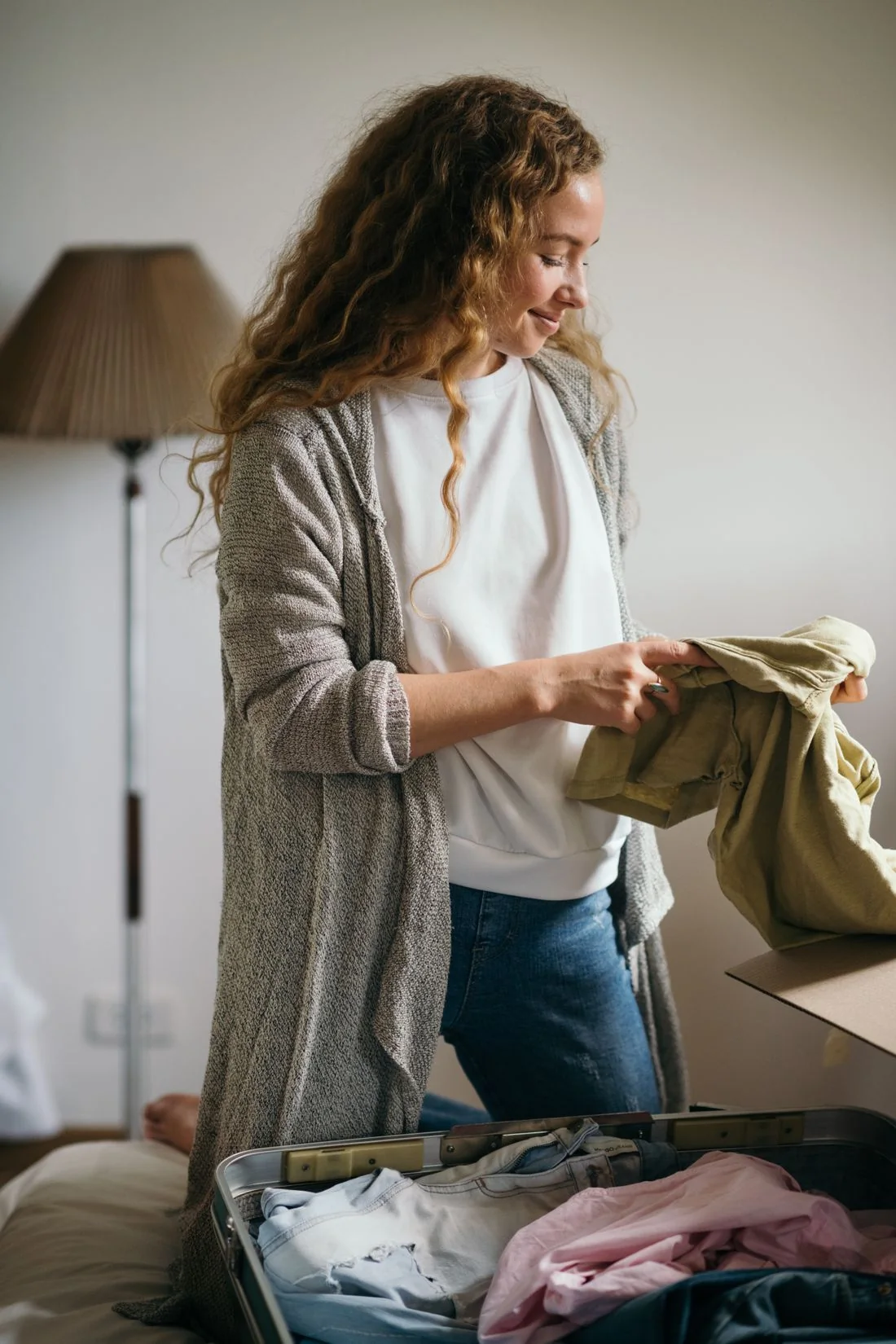 A person folding clothing beside an open suitcase in a bedroom.