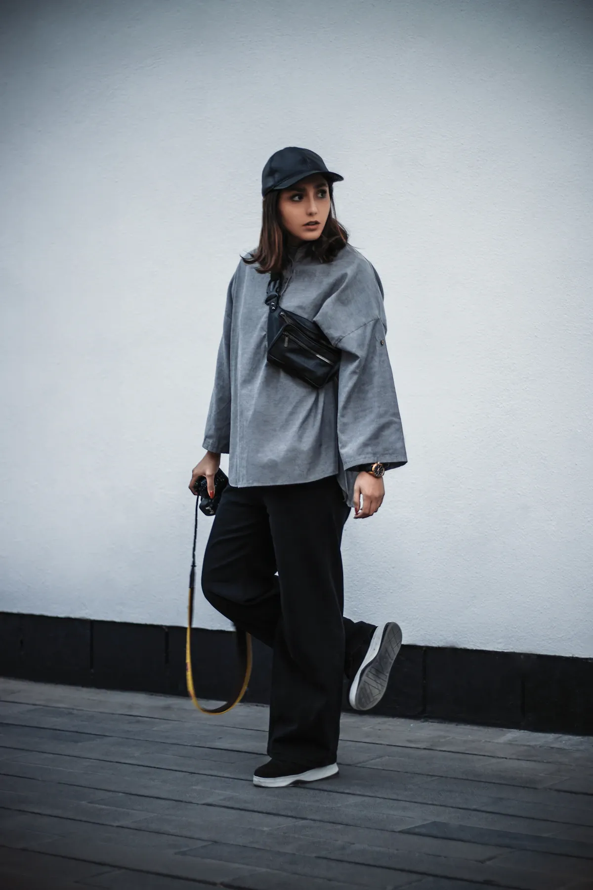 A woman in a gray shirt, black trousers and a baseball cap outdoors